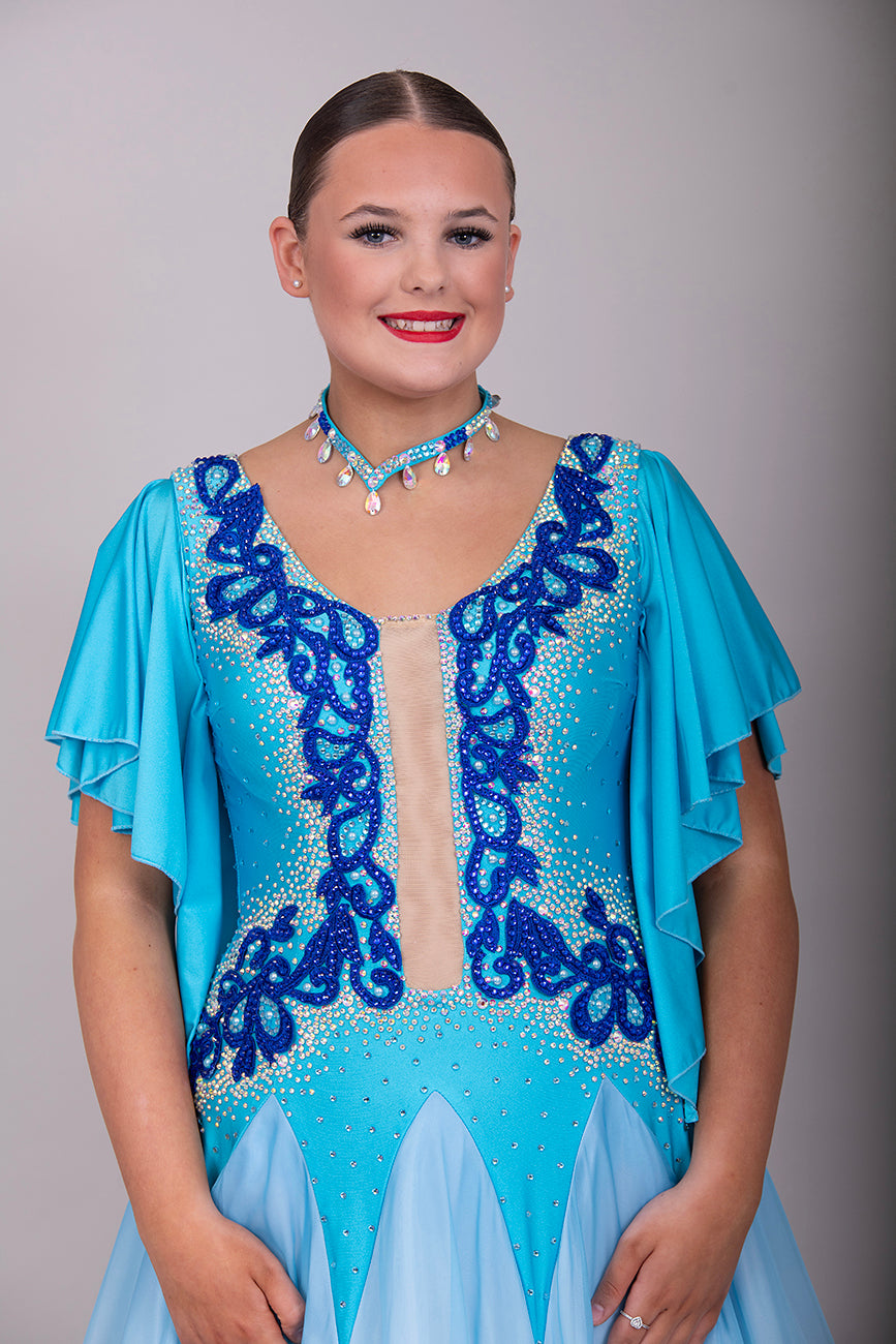 034 Turquoise & White ombré Ballroom Dress. Feature floaty sleeves & flesh panel detail to the chest. Decorated with royal blue motifs. Stoned in sapphire, light sapphire & AB