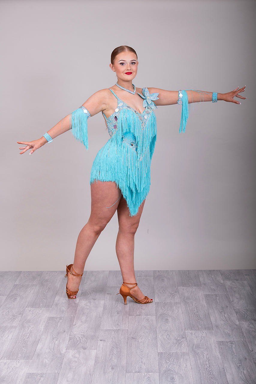 001 Turquoise Blue Competition Latin Dance Dress. Very full Fringes. 3D flower detail to the left shoulder. Cones with fringed armbands and bracelets. Decorated with silver mirrors & AB stones.
