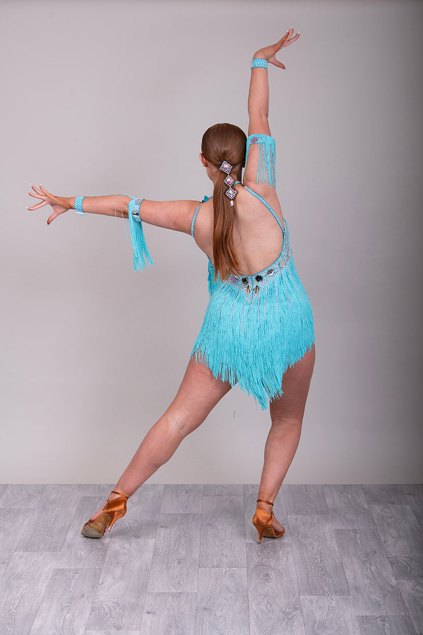 001 Turquoise Blue Competition Latin Dance Dress. Very full Fringes. 3D flower detail to the left shoulder. Cones with fringed armbands and bracelets. Decorated with silver mirrors & AB stones.