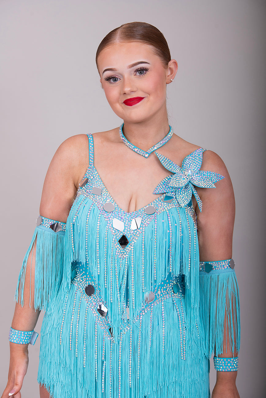 001 Turquoise Blue Competition Latin Dance Dress. Very full Fringes. 3D flower detail to the left shoulder. Cones with fringed armbands and bracelets. Decorated with silver mirrors & AB stones.