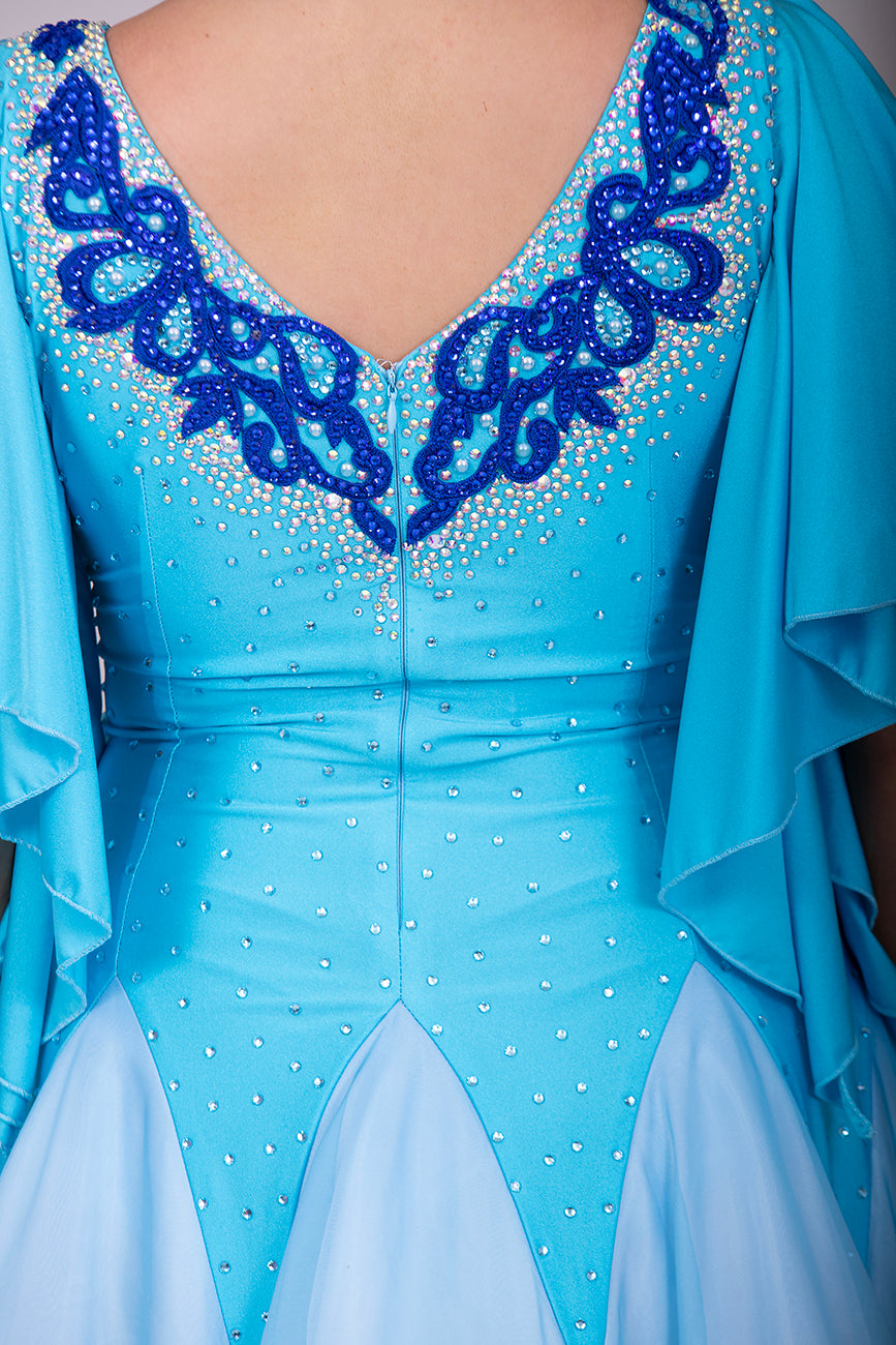 034 Turquoise & White ombré Ballroom Dress. Feature floaty sleeves & flesh panel detail to the chest. Decorated with royal blue motifs. Stoned in sapphire, light sapphire & AB
