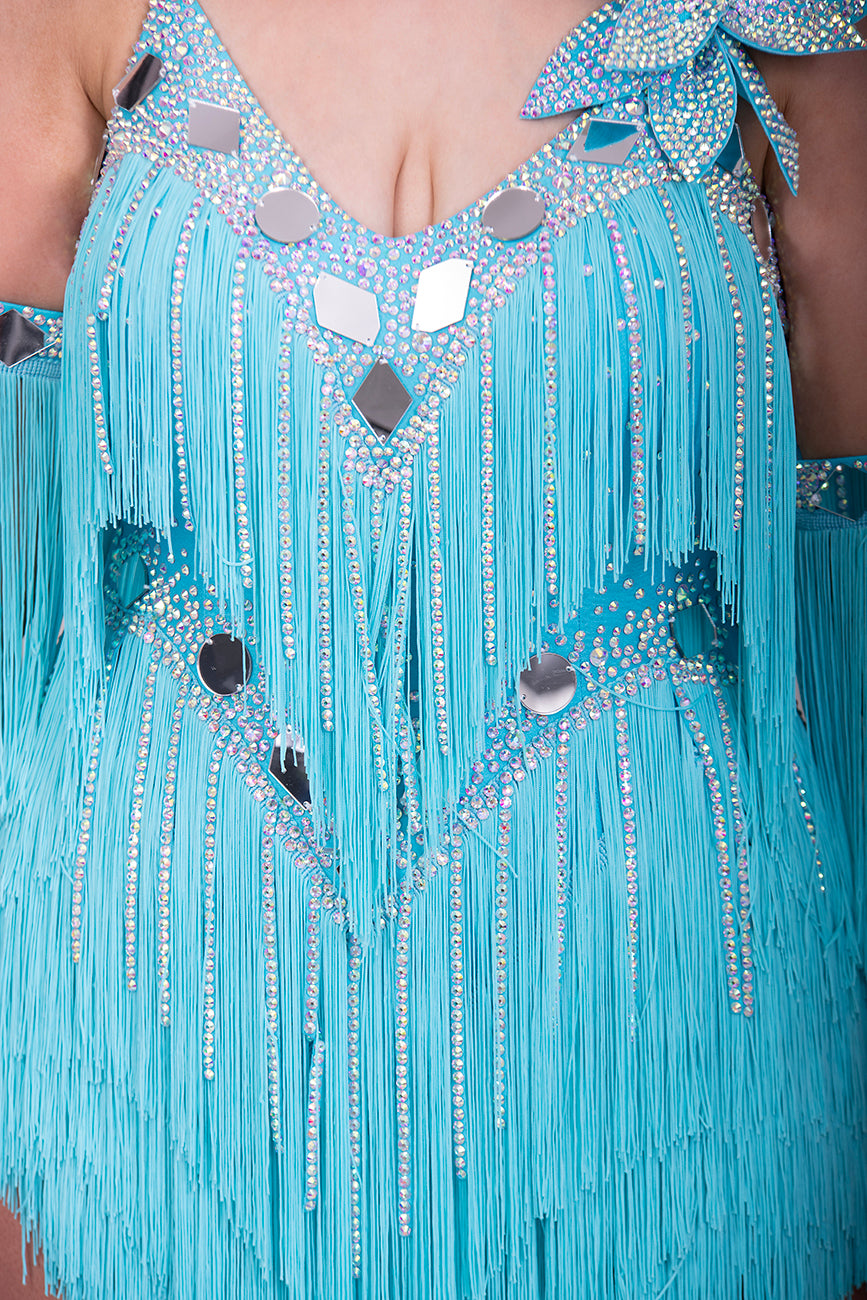 001 Turquoise Blue Competition Latin Dance Dress. Very full Fringes. 3D flower detail to the left shoulder. Cones with fringed armbands and bracelets. Decorated with silver mirrors & AB stones.