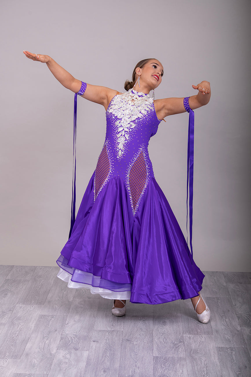056 Purple Halter Neck Ballroom Dress. White lace detail front/back bodice. Purple fishnet panel on front. Decorated in purple & AB stones. Underskirts in White with exposed satin skirts to one side