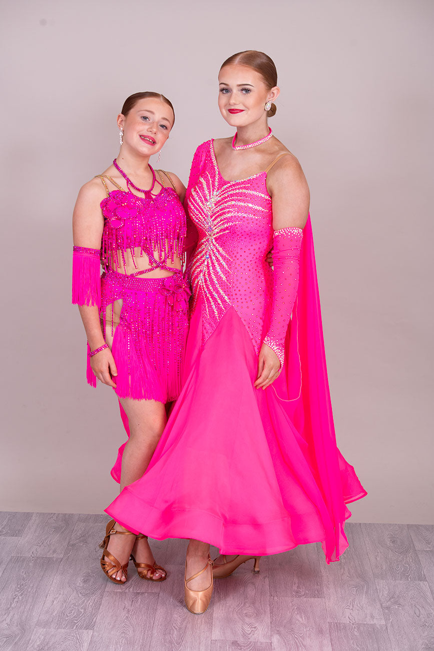 (BUDGET)11 Rose Pink Competition Latin Dance Dress. Flower detail to the chest & Hip. Fringed skirt with open side detail. Fringed arm cuffs & detailed necklace. Joined by crossover straps