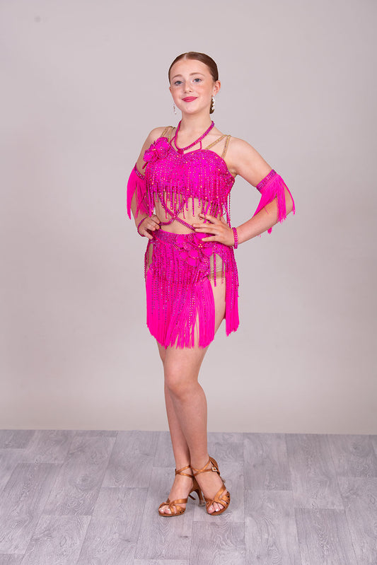 (BUDGET)11 Rose Pink Competition Latin Dance Dress. Flower detail to the chest & Hip. Fringed skirt with open side detail. Fringed arm cuffs & detailed necklace. Joined by crossover straps