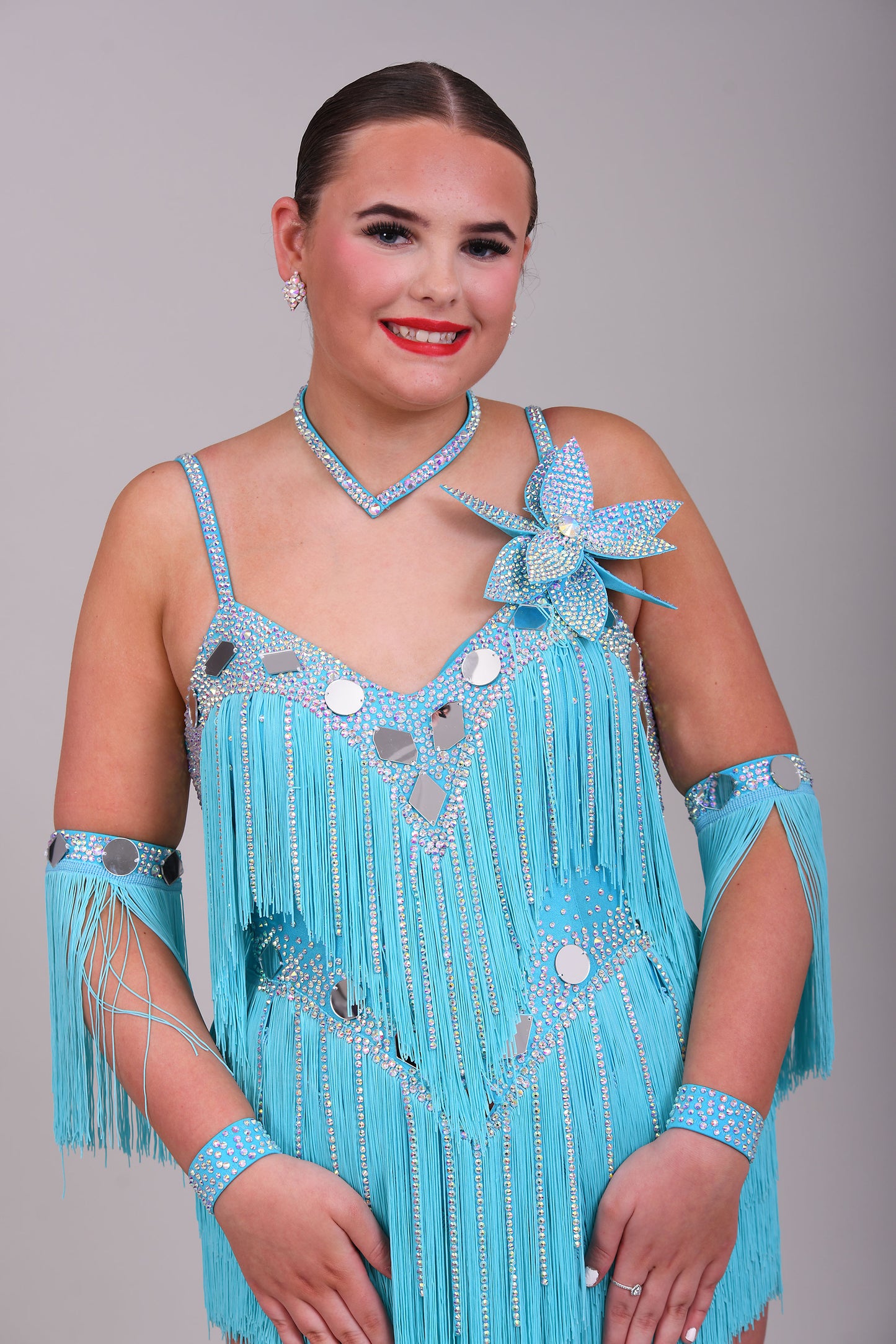 001 Turquoise Blue Competition Latin Dance Dress. Very full Fringes. 3D flower detail to the left shoulder. Cones with fringed armbands and bracelets. Decorated with silver mirrors & AB stones.