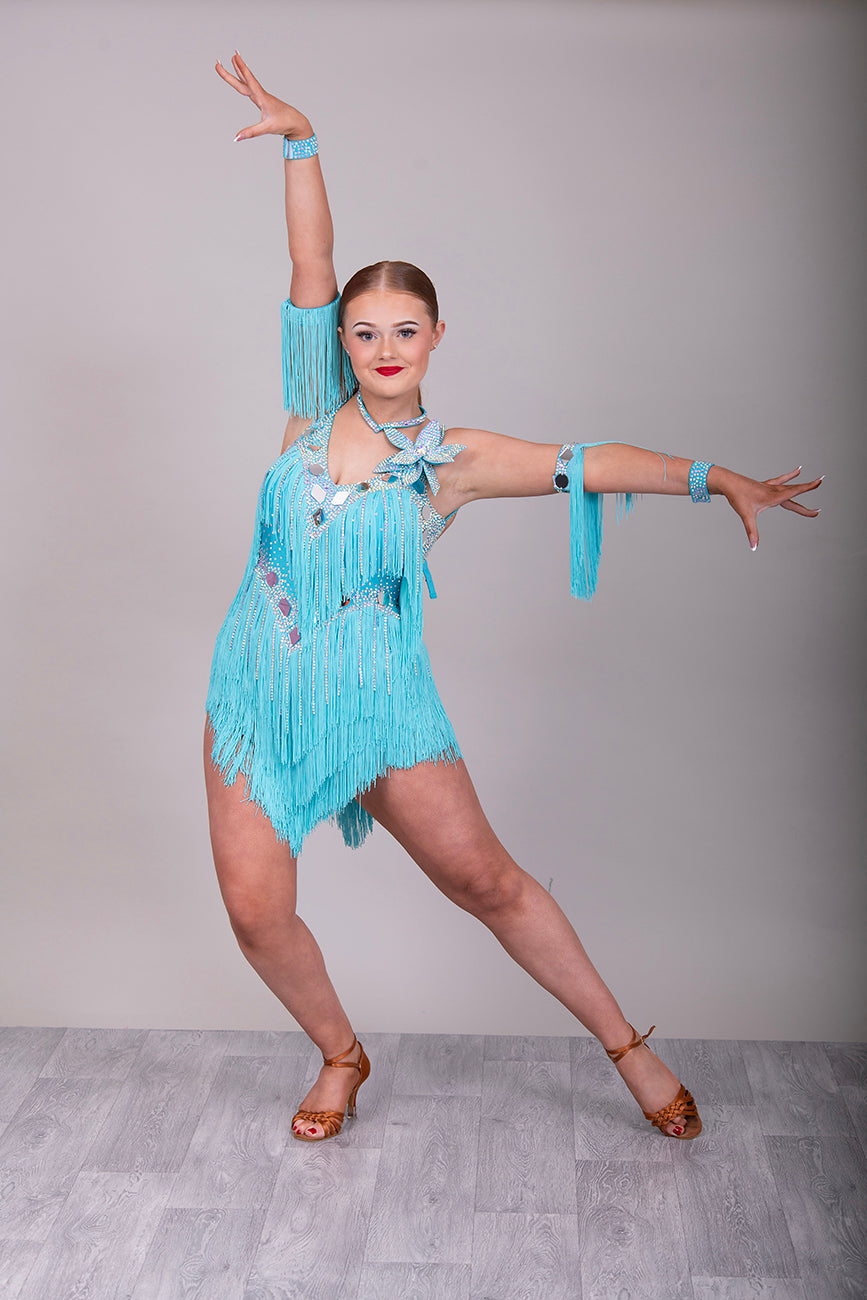 001 Turquoise Blue Competition Latin Dance Dress. Very full Fringes. 3D flower detail to the left shoulder. Cones with fringed armbands and bracelets. Decorated with silver mirrors & AB stones.