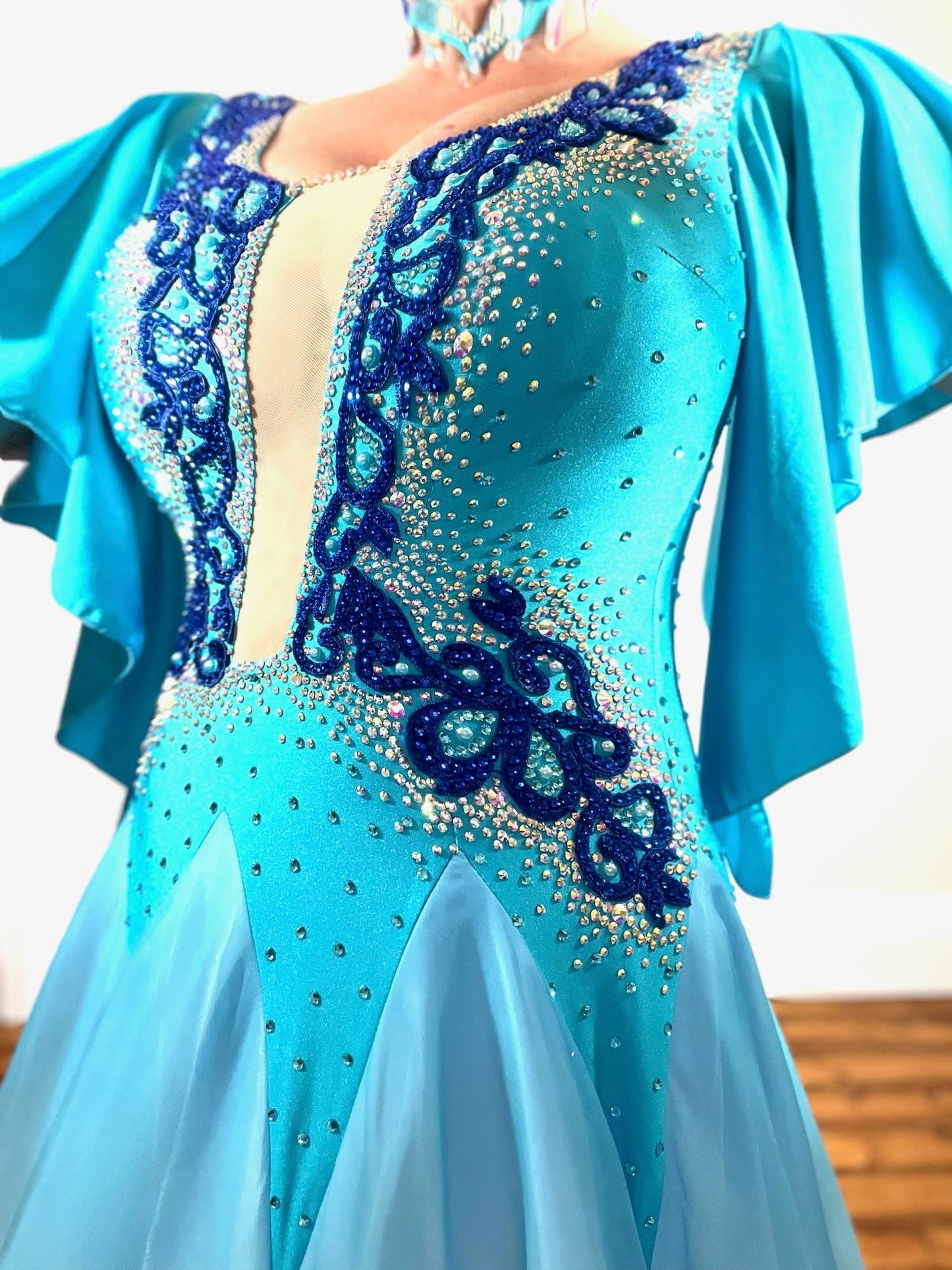034 Turquoise & White ombré Ballroom Dress. Feature floaty sleeves & flesh panel detail to the chest. Decorated with royal blue motifs. Stoned in sapphire, light sapphire & AB