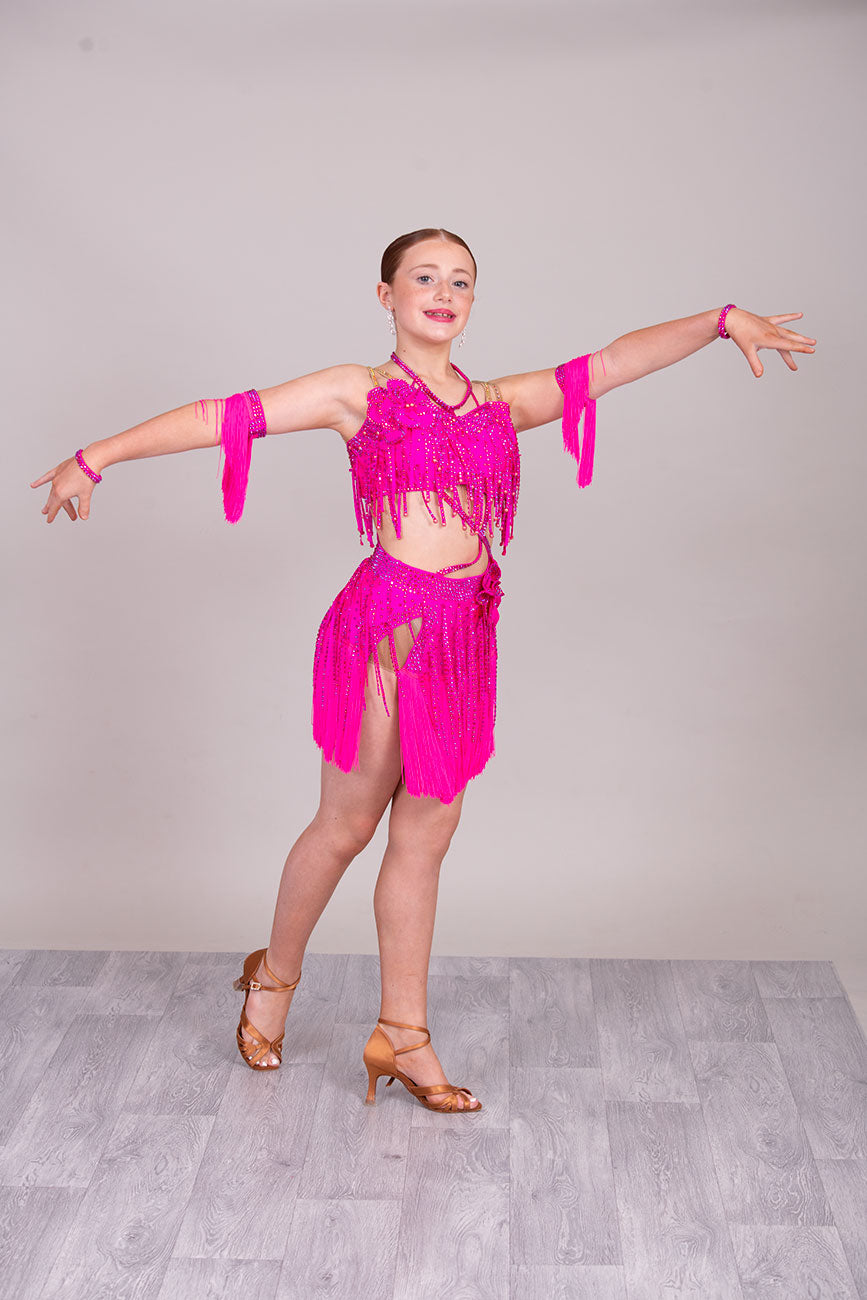 (BUDGET)11 Rose Pink Competition Latin Dance Dress. Flower detail to the chest & Hip. Fringed skirt with open side detail. Fringed arm cuffs & detailed necklace. Joined by crossover straps