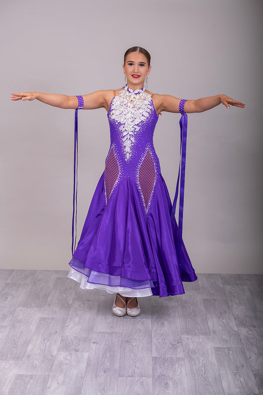 056 Purple Halter Neck Ballroom Dress. White lace detail front/back bodice. Purple fishnet panel on front. Decorated in purple & AB stones. Underskirts in White with exposed satin skirts to one side