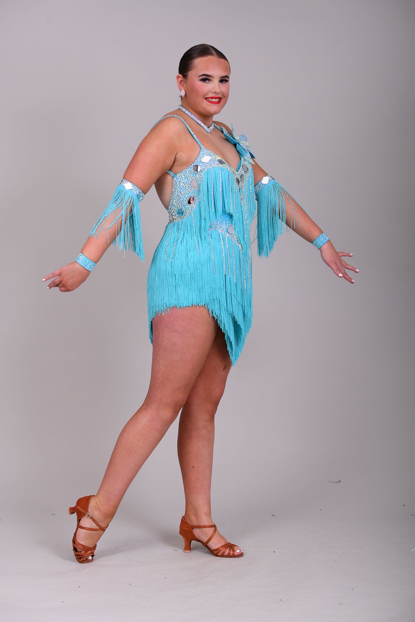 001 Turquoise Blue Competition Latin Dance Dress. Very full Fringes. 3D flower detail to the left shoulder. Cones with fringed armbands and bracelets. Decorated with silver mirrors & AB stones.