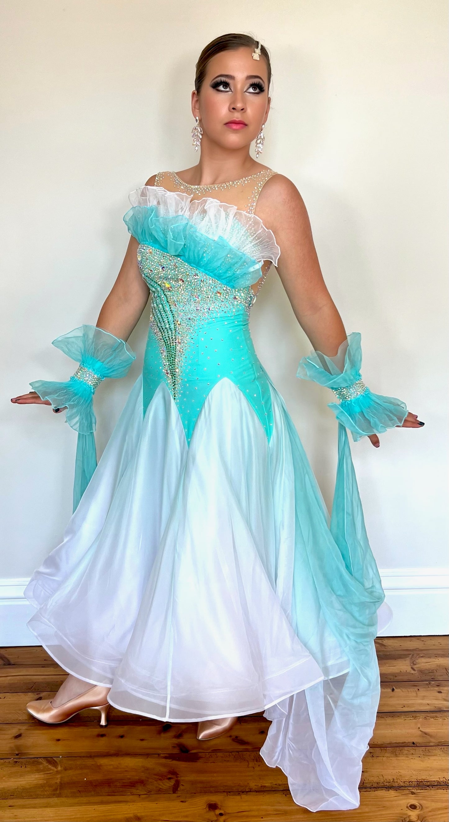 043 Bright Aqua & Green & White Ombré Ballroom Dress. Organza frill detailing to the upper chest. Decorative organza cuffs with ombré floats attached to the back on one side. Separate hanging float to the opposite side. Decorated in AB stones.