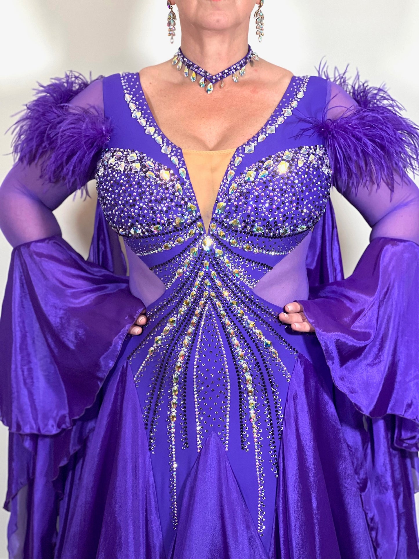 287 Stunning Purple Ballroom Dance Dress. Ostrich feather detail to the upper arm with floaty sleeves from the elbow(finger loop can be added). High back for wearing own bra. Stoned in AB, light Amethyst & Amethyst.