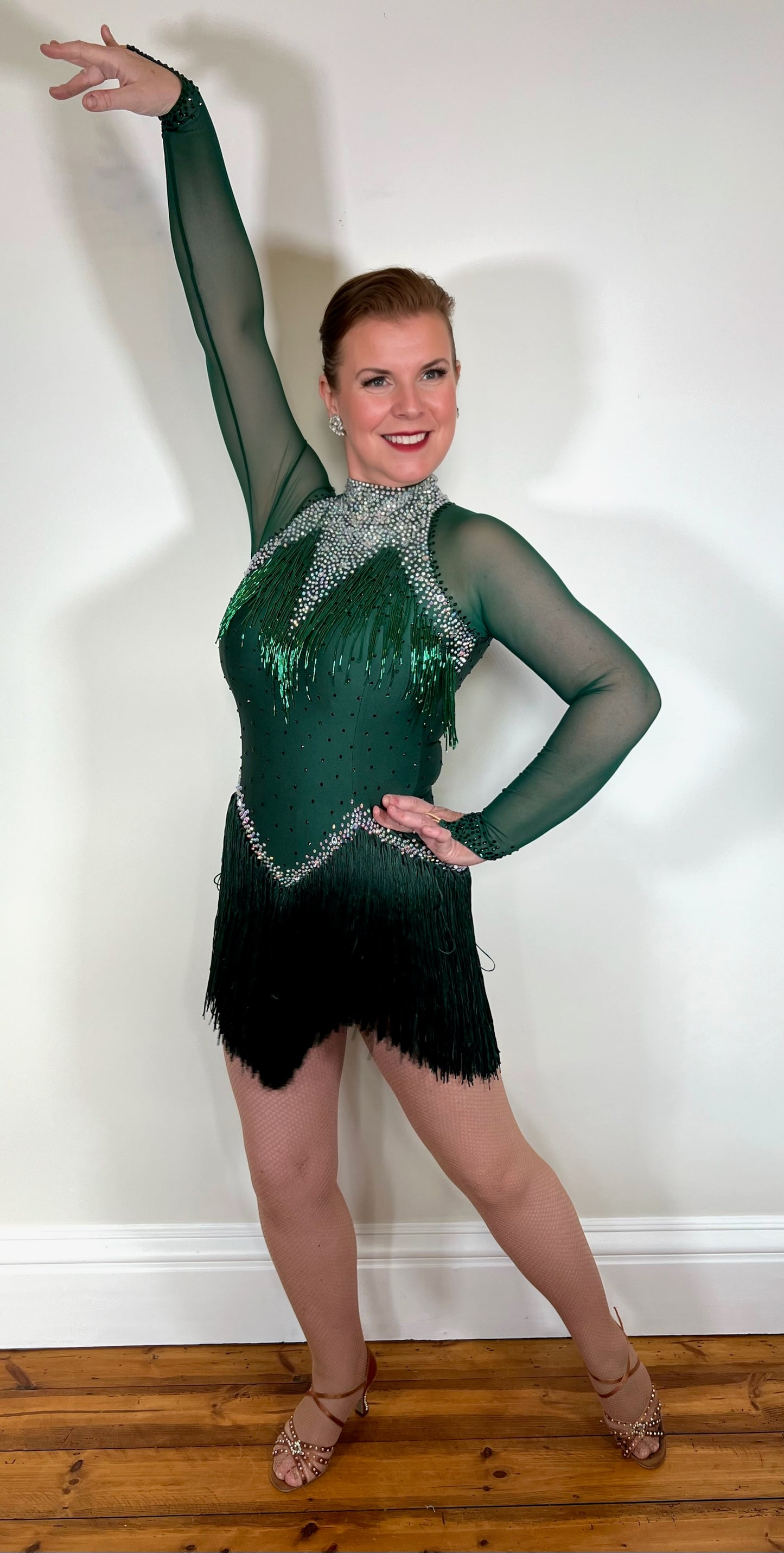 051 Forest Green Competition Latin Dance Dress. Bead droppers to the upper chest are with high neck and stoned chest detail. Heavy fringing to the skirt. Long sleeved and filled in mesh back. Stoned in emerald green & AB