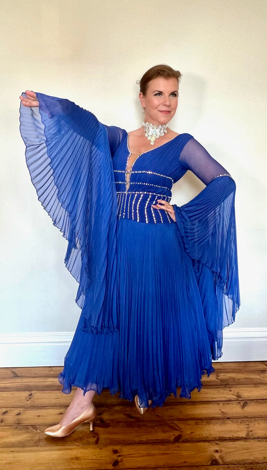 187 Royal Blue Pleated Skirt Ballroom Dress. Full circle pleated cuff detail. Mesh sleeves. Plunge detail bodice with flesh panel. All stones in AB