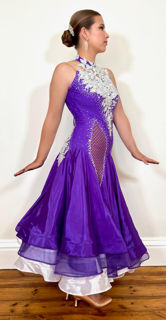 056 Purple Halter Neck Ballroom Dress. White lace detail front/back bodice. Purple fishnet panel on front. Decorated in purple & AB stones. Underskirts in White with exposed satin skirts to one side
