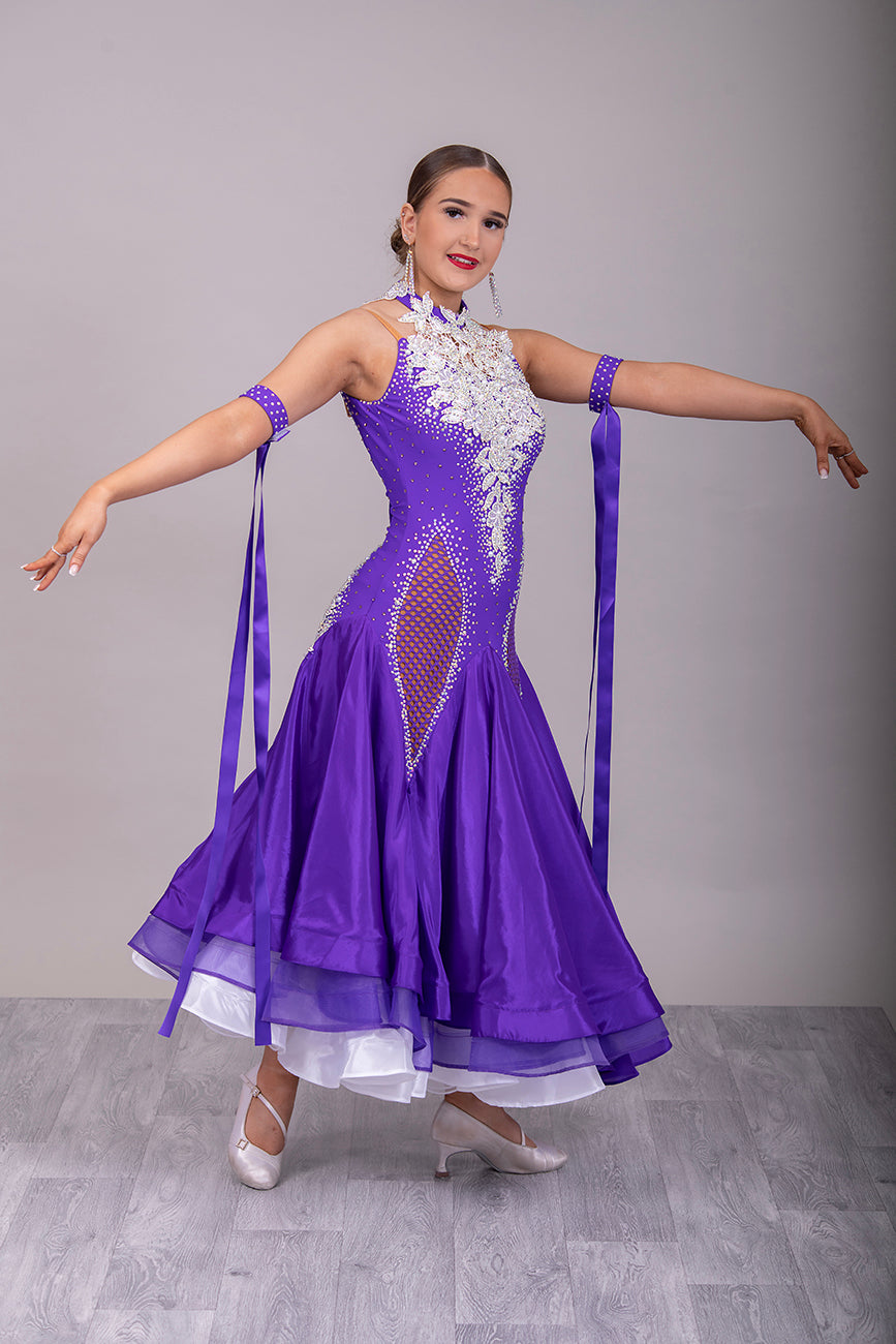 056 Purple Halter Neck Ballroom Dress. White lace detail front/back bodice. Purple fishnet panel on front. Decorated in purple & AB stones. Underskirts in White with exposed satin skirts to one side