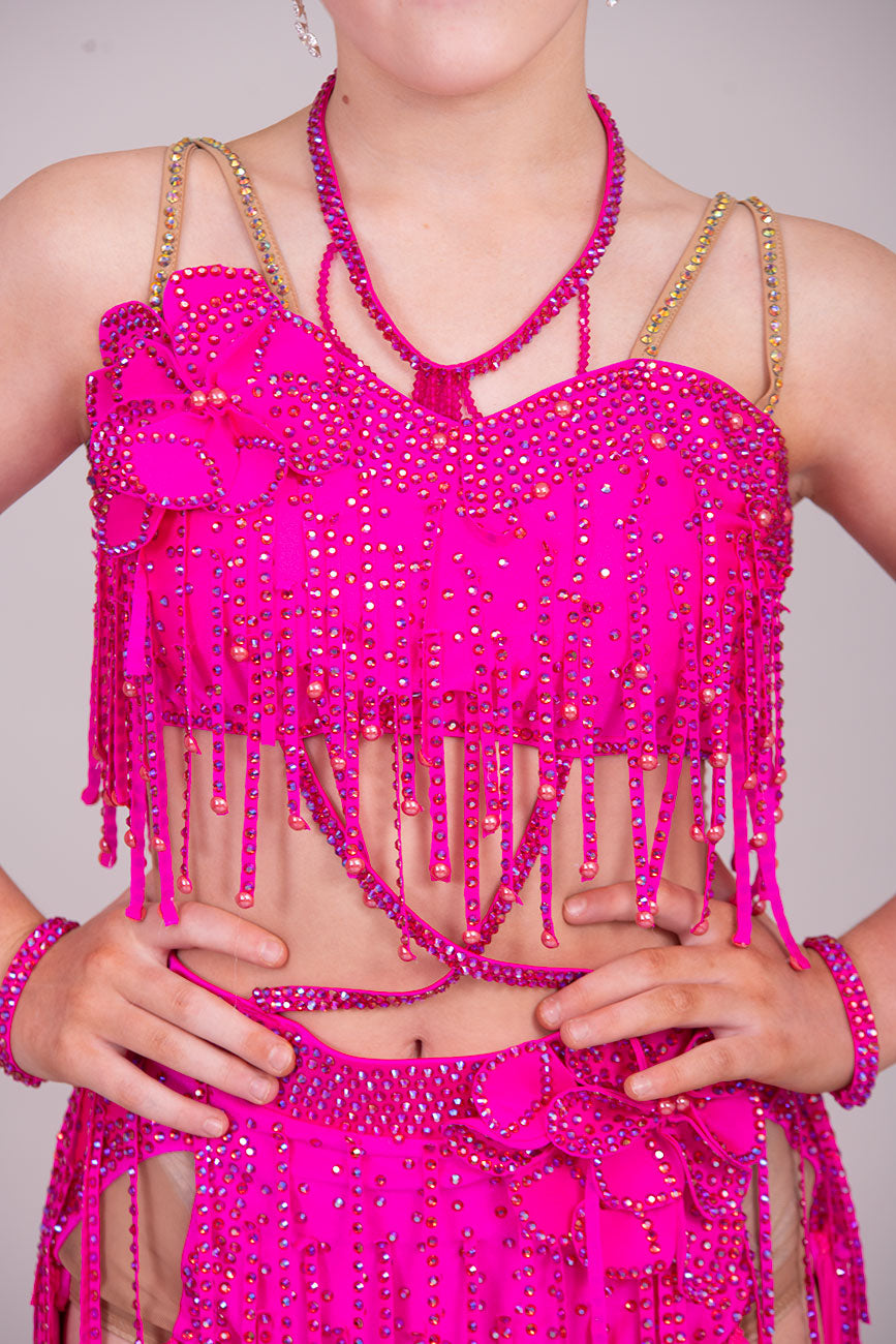 (BUDGET)11 Rose Pink Competition Latin Dance Dress. Flower detail to the chest & Hip. Fringed skirt with open side detail. Fringed arm cuffs & detailed necklace. Joined by crossover straps