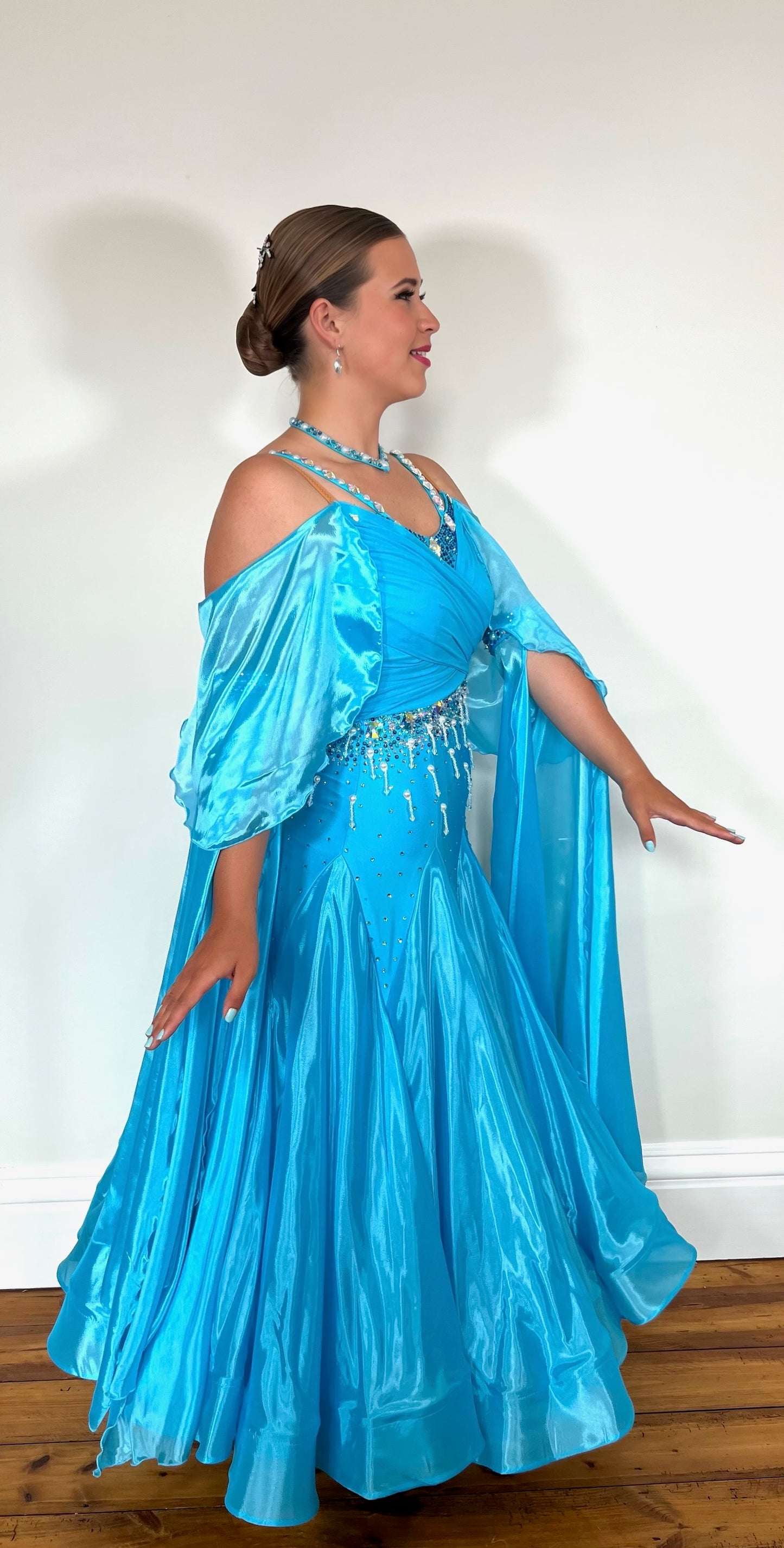 322 Paradise Blue Ballroom Dress with shoulder drapes. Comes with separate arm cuff floats. Decorated with Pearls, blue and AB stones. Detailed pearl strings to back