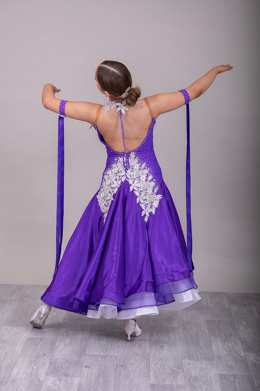 056 Purple Halter Neck Ballroom Dress. White lace detail front/back bodice. Purple fishnet panel on front. Decorated in purple & AB stones. Underskirts in White with exposed satin skirts to one side