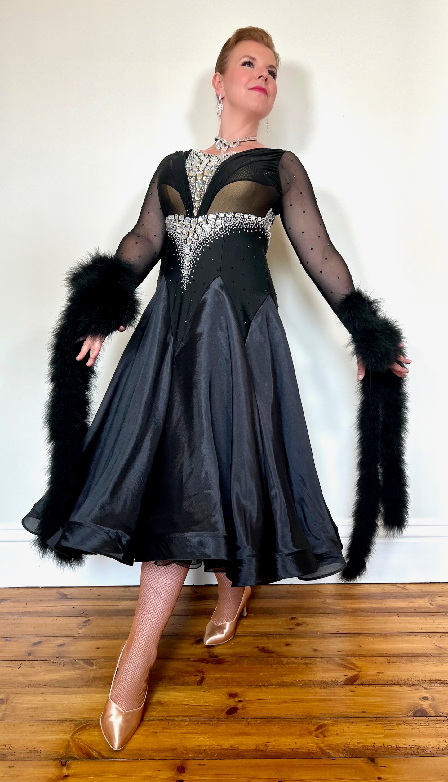 324 Black Ballroom Dress with feather floats to the wrist. Rouched detail to the chest area. Heavily decorated stoning to the front & back in AB. High back.