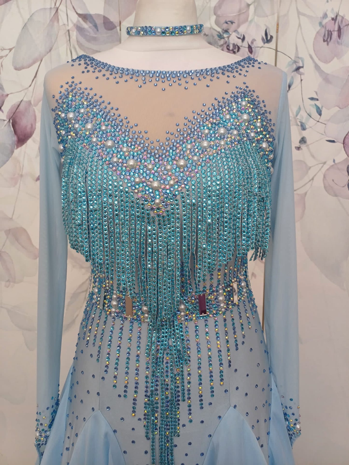 208 Baby Blue boat neck Ballroom Dress with flesh panel to the back. Stoned fringe detail to the chest area. Stoned waist detail to the front & back. Boat neck with flesh panel to the back. Decorated with AB, light sapphire & sapphire stones