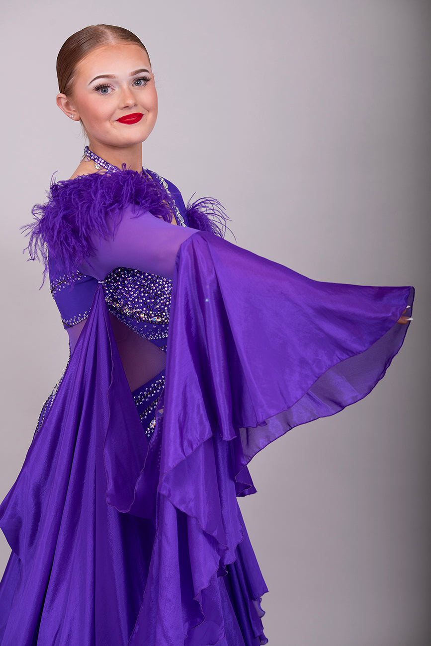 287 Stunning Purple Ballroom Dance Dress. Ostrich feather detail to the upper arm with floaty sleeves from the elbow(finger loop can be added). High back for wearing own bra. Stoned in AB, light Amethyst & Amethyst.