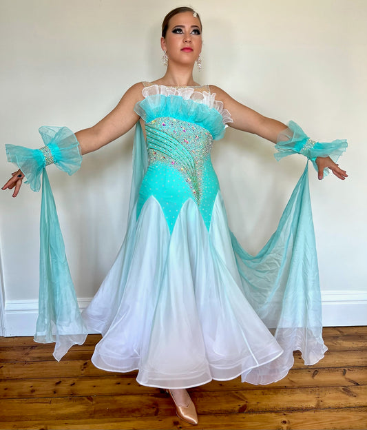 043 Bright Aqua/White Ombré Ballroom Dress. Organza frill detailing to chest. Decorative organza cuffs with ombré floats attached to the back on one side. Separate hanging float to the opposite side. Decorated in AB stones.