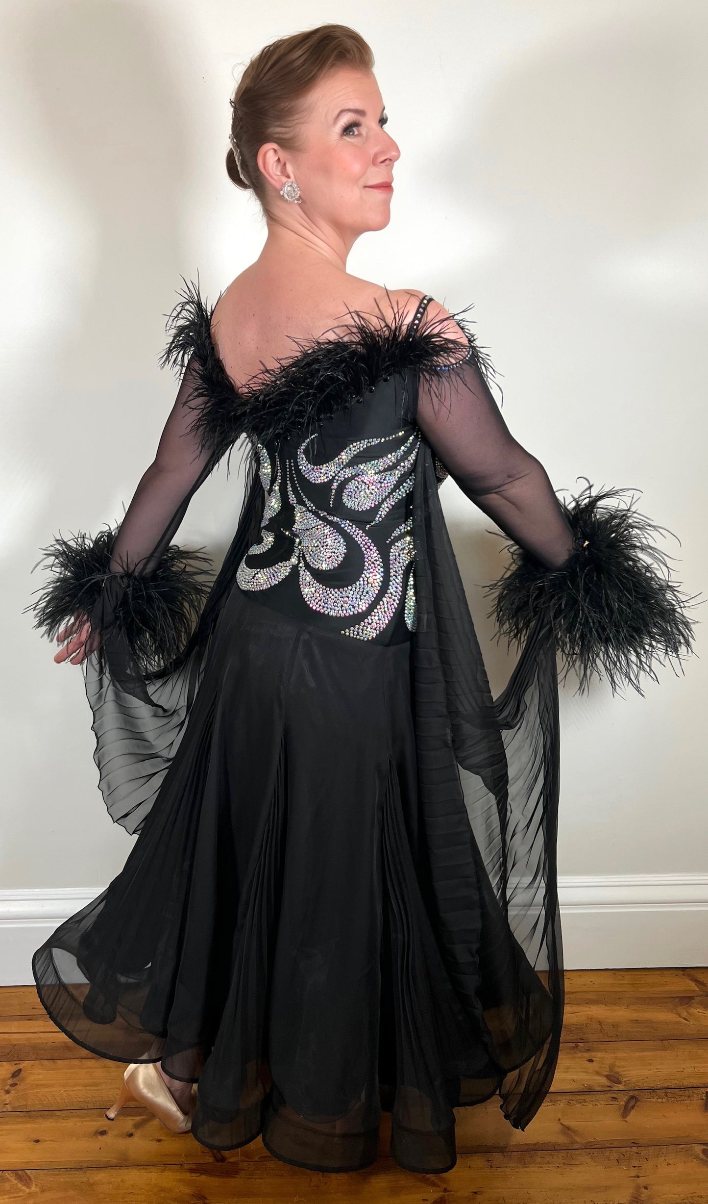 053 Black Competition Ballroom Dance Dress. Heavily stoned in AB with Ostrich feathers to the upper chest area. Detachable floats with ostrich feather cuffs.