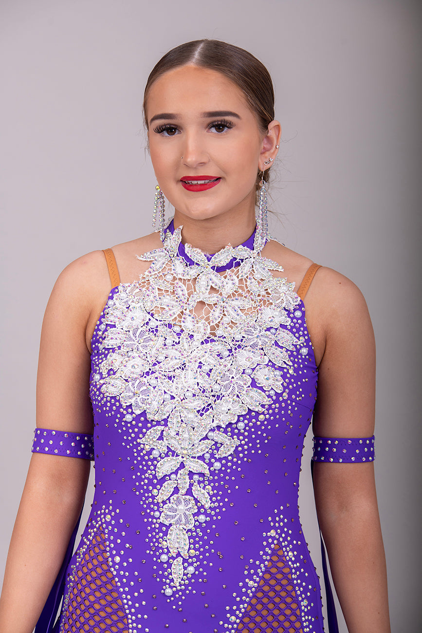 056 Purple Halter Neck Ballroom Dress. White lace detail front/back bodice. Purple fishnet panel on front. Decorated in purple & AB stones. Underskirts in White with exposed satin skirts to one side