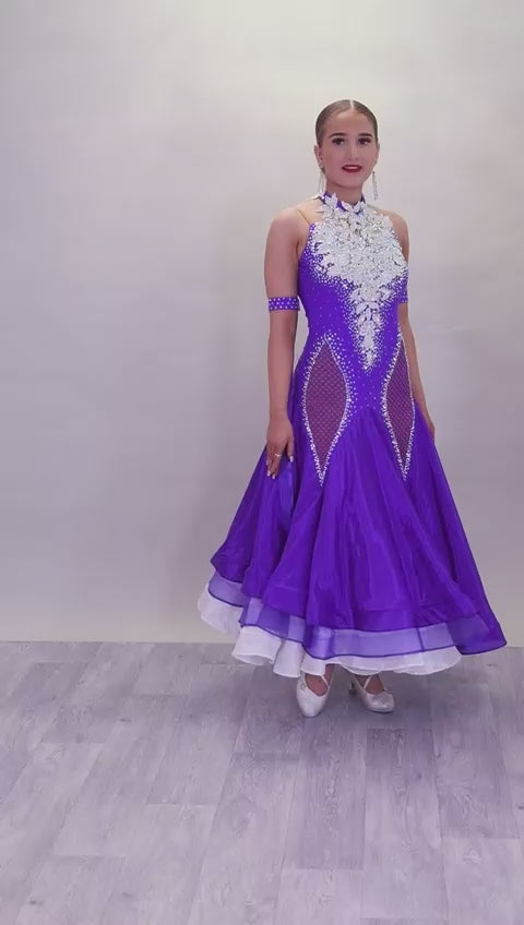 056 Purple Halter Neck Ballroom Dress. White lace detail front/back bodice. Purple fishnet panel on front. Decorated in purple & AB stones. Underskirts in White with exposed satin skirts to one side